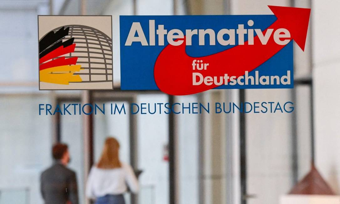 Pessoas caminham atrás de parede de vidro com logo da Alternativa para a Alemanha no Budenstag, o Parlamento do país Foto: TOBIAS SCHWARZ / AFP