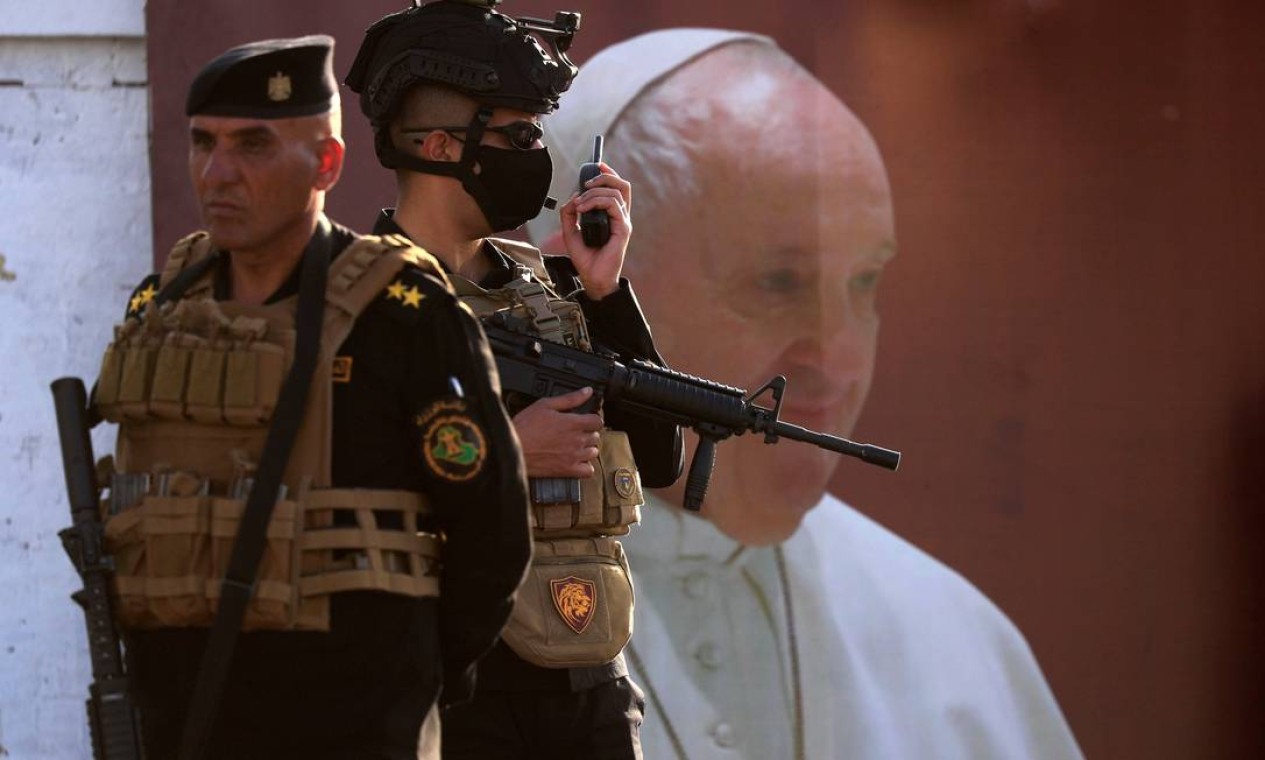 Membros das forças de segurança iraquianas ficam de guarda perto de um pôster do Papa Francisco antes de sua chegada à catedral siro-católica de "Nossa Senhora da Salvação" em Bagdá Foto: THAIER AL-SUDANI / REUTERS