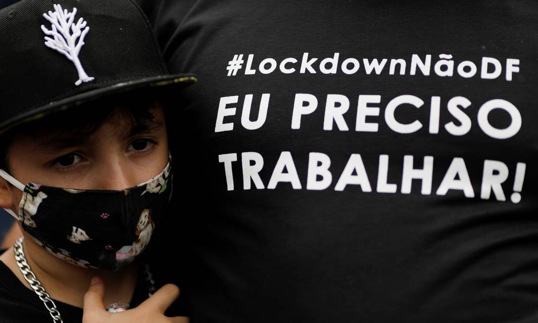 Criança usando máscara abraça adulto que veste camisa de protesto contra o lockdown em Brasília, apesar dos números da pandemia Foto: UESLEI MARCELINO / REUTERS - 28/02/2021
