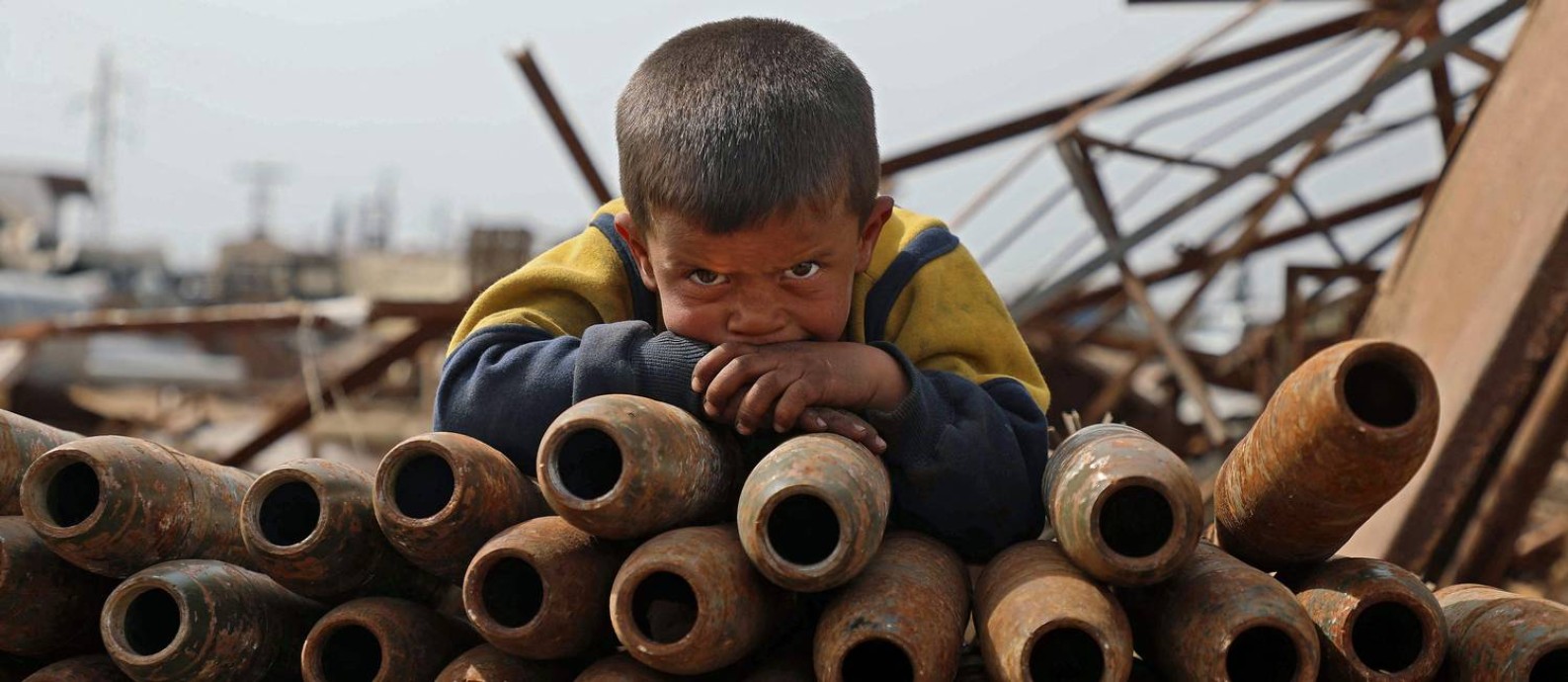 Criança síria posa sobre pilha de projéteis neutralizados em ferro-velho nos arredores de Maaret Misrin, na província de Idlib Foto: AAREF WATAD / AFP/10-03-2021