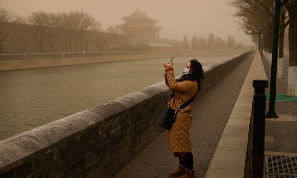 Uma mulher usa um telefone celular para tirar fotos fora da Cidade Proibida durante uma tempestade de areia em Pequim Foto: WANG ZHAO / AFP