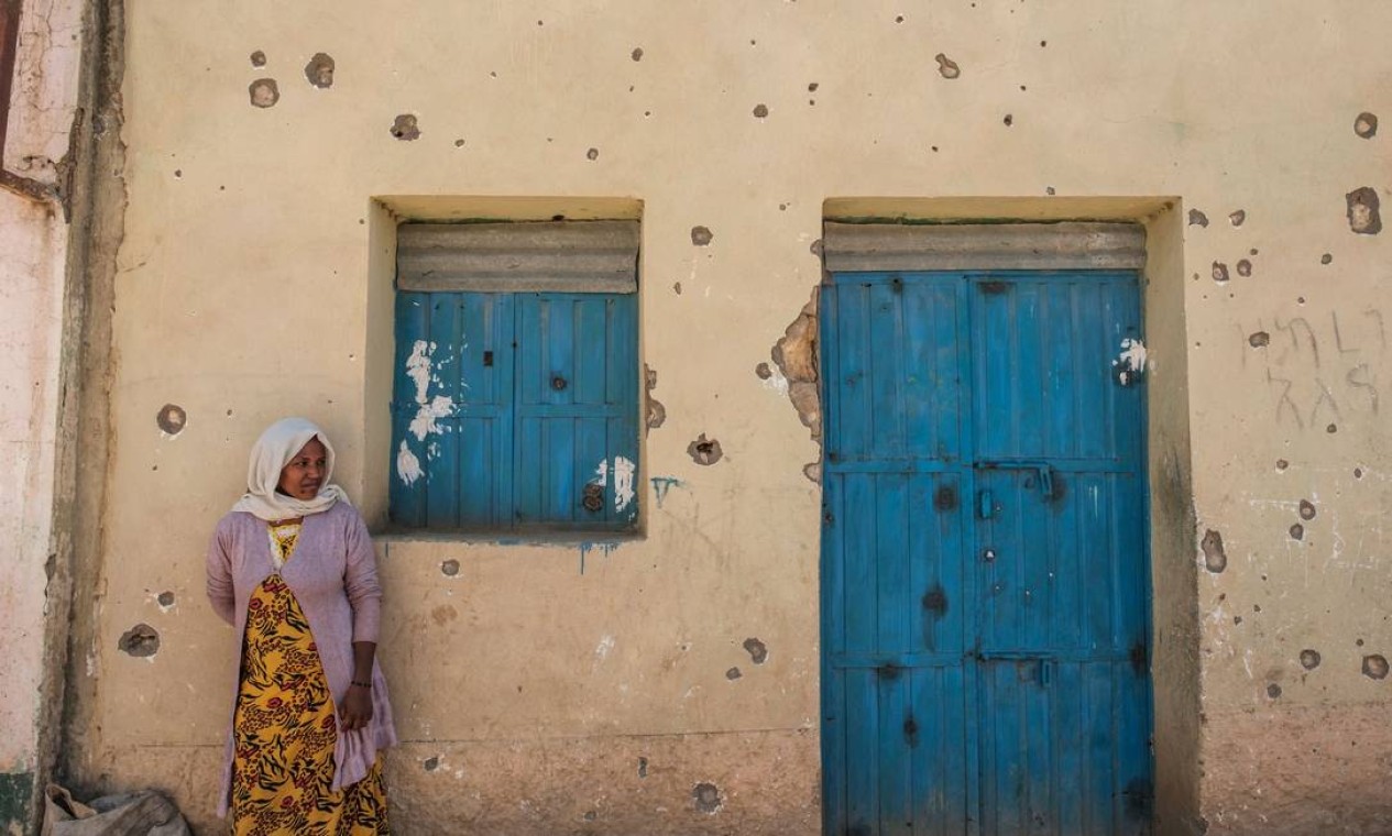Mulher se apoia na parede de uma casa cravejada por marcas de tiros, em Wukro, ao norte de Mekele. Desde novembro, a cidade tem sido fortemente patrulhada por soldados, inicialmente eritreus, agora principalmente etíopes, cujos abusos alimentam um fluxo constante de vítimas civis e alimentam a raiva do ganhador do Prêmio Nobel da Paz, primeiro-ministro Abiy Ahmed Ali Foto: EDUARDO SOTERAS / AFP