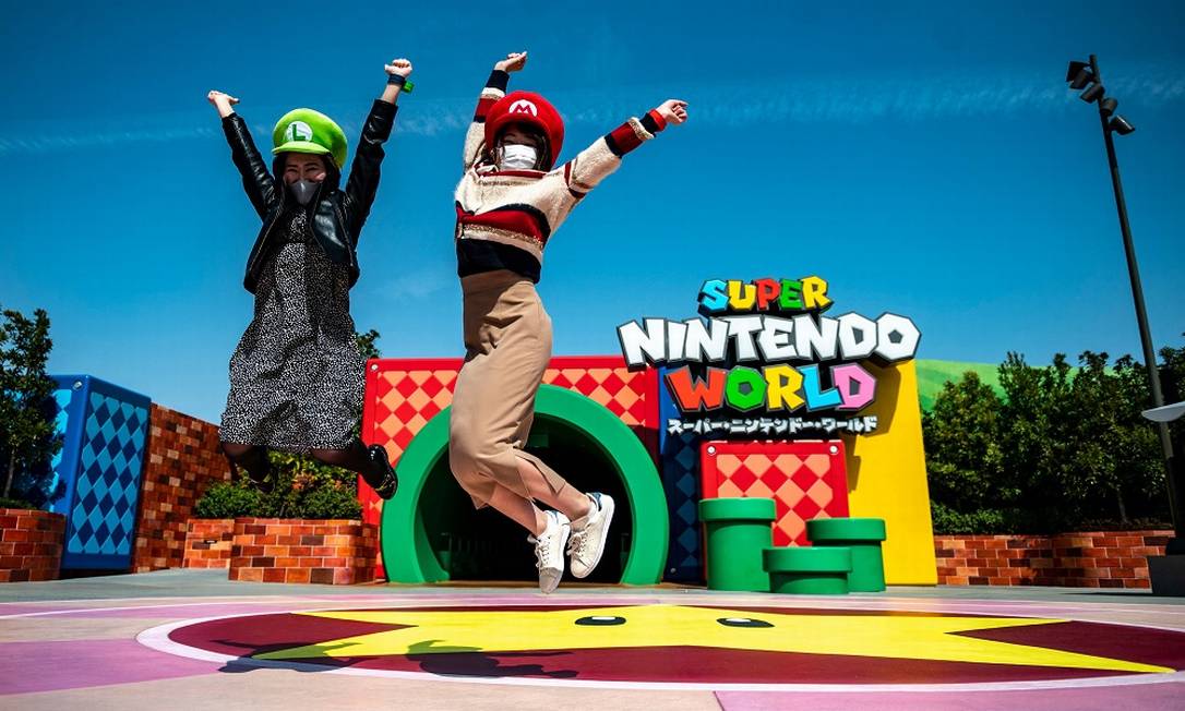 Duas visitantes com seus chapeus de Mario e Luigi saltam em frente ao túnel em forma de cano que dá acesso à área temática Super Nintendo World, do Universal Studio Japan Foto: PHILIP FONG / AFP