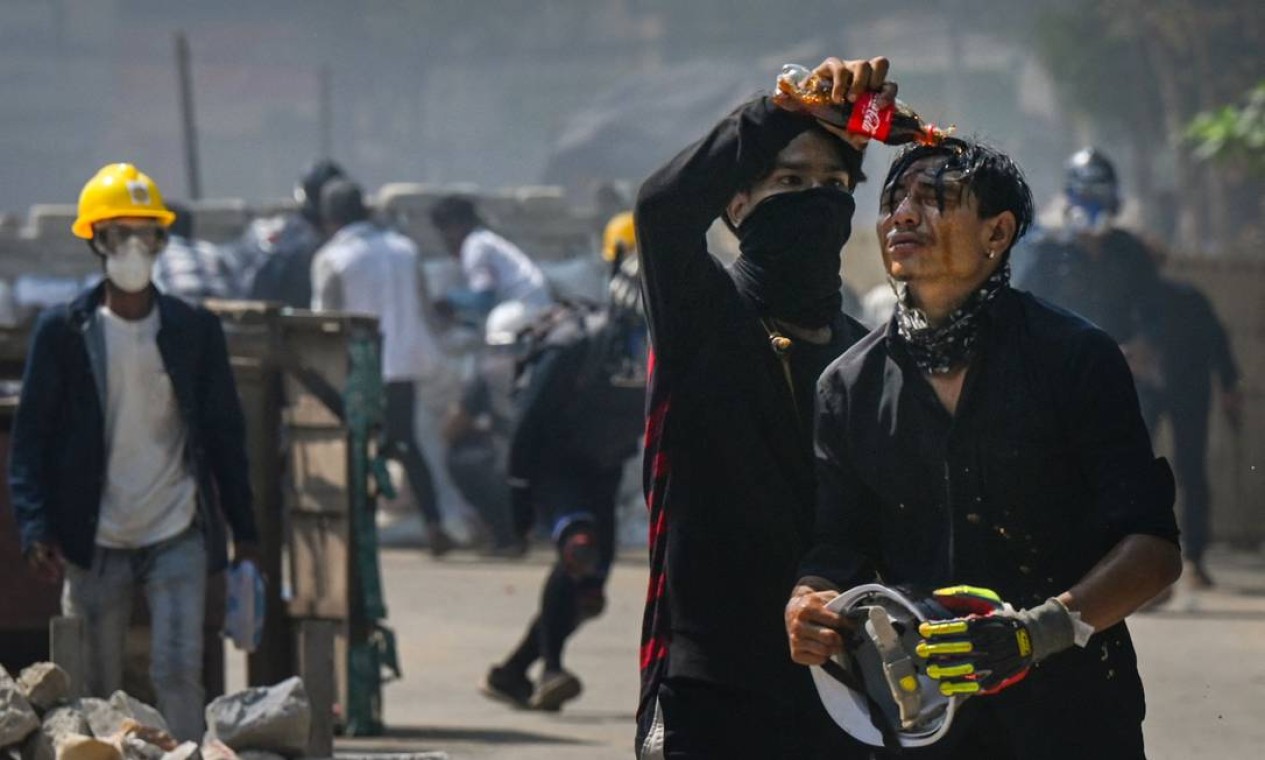 Manifestante derrama Coca-Cola no rosto de um companheiro para diminuir os efeitos do gás lacrimogêneo disparado pelas forças de segurança em uma manifestação contra o golpe militar no município de Thaketa, Mianmar Foto: STR / AFP