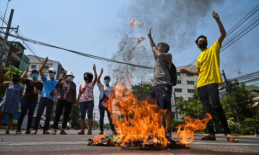 Manifestantes fazem saudação enquanto queimam Consituição de Mianmar em um protesto contra o golpe militar que afeta o país Foto: STR / AFP