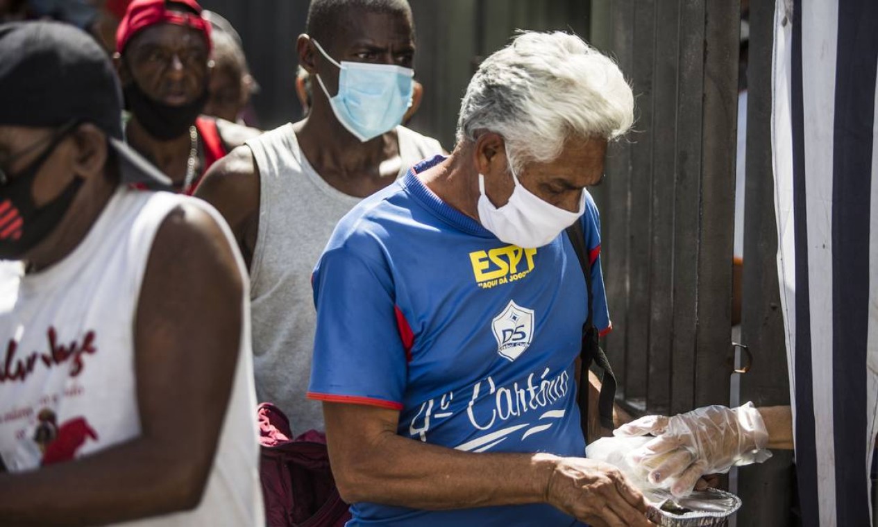 Homem usando máscara de proteção recebe refeição no Centro do Rio Foto: Guito Moreto / Agência O Globo
