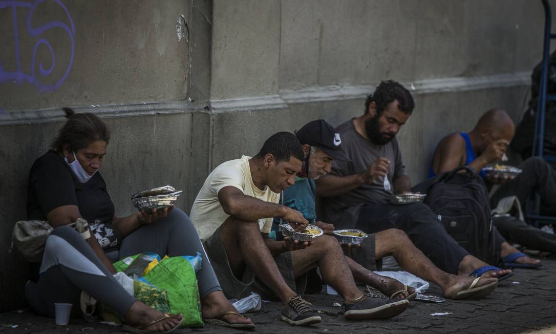 Pessoas que receberam refeição se sentam à sombra, na calçada, para comer no Centro do Rio Foto: Guito Moreto / Agência O Globo