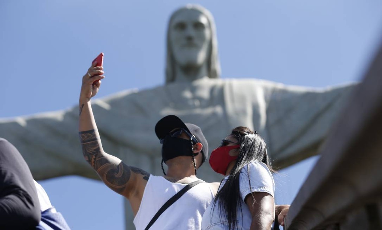 Casal usando máscara, de uso obrigatório durante a visita, faz selfie em frente à estátua do Cristo, que reabriu às 12h desta sexta-feira (5) para visitação Foto: Roberto Moreyra / Agência O Globo