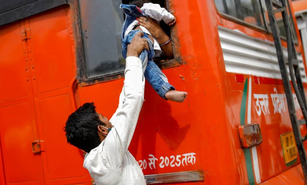 Trabalhador migrante passa seu filho pela janela de um ônibus de volta para sua aldeia, depois que o governo de Delhi ordenou bloqueio de seis dias para limitar a propagação da doença do coronavírus, em Ghaziabad, Índia Foto: ADNAN ABIDI / REUTERS