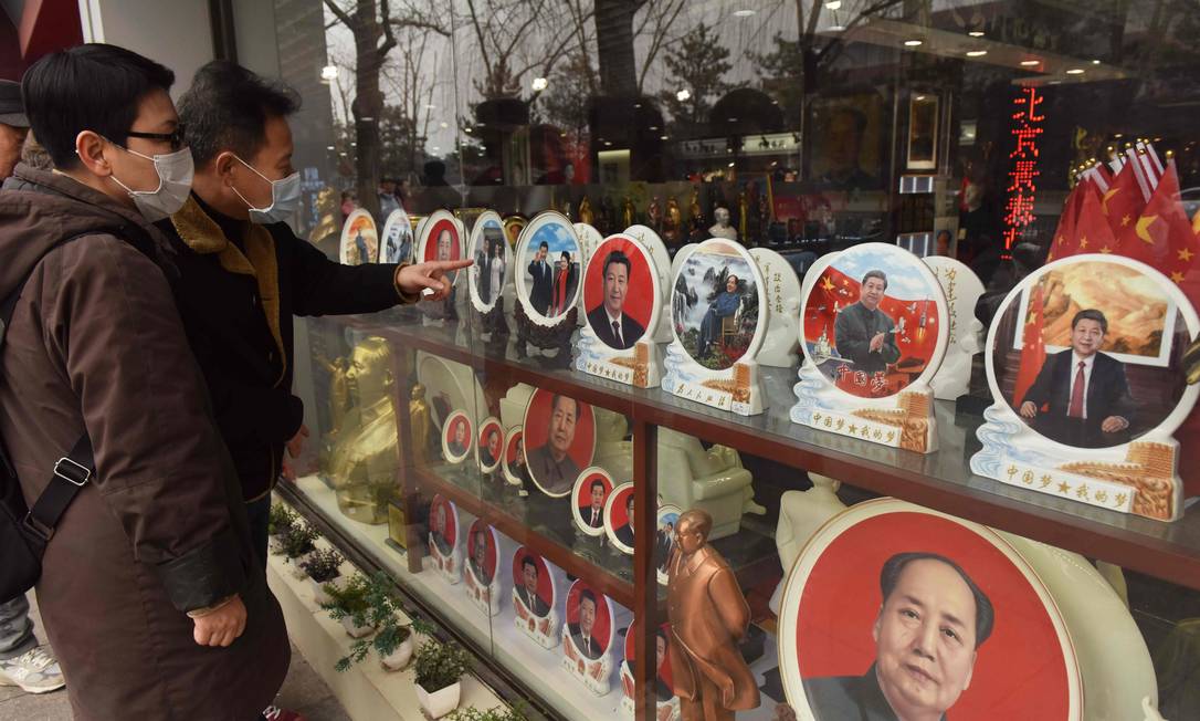 Pessoas olham para placas decorativas com imagens de líderes chineses, incluindo o atual presidente Xi Jinping e o fundador do PCC Mao Zedong em vitrine de loja em Pequim Foto: GREG BAKER / AFP/27-02-2018