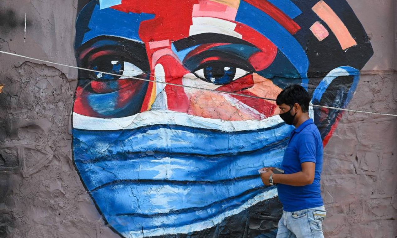 Pedestre passa por um grafite de pessoa usando uma máscara protetora, em Mumbai Foto: PUNIT PARANJPE / AFP