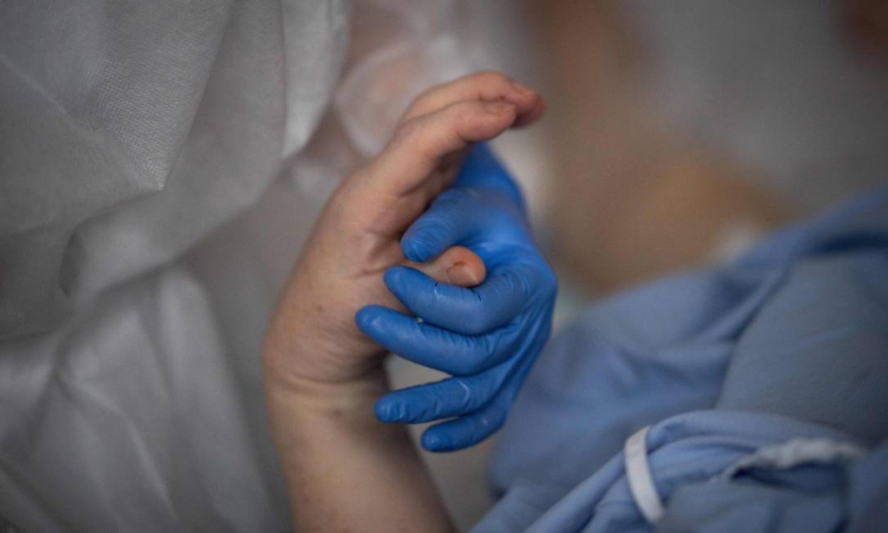 Um membro da equipe médica segura a mão de um paciente infectado com Covid-19 em Vannes, na França Foto: LOIC VENANCE / AFP - 20/04/2021