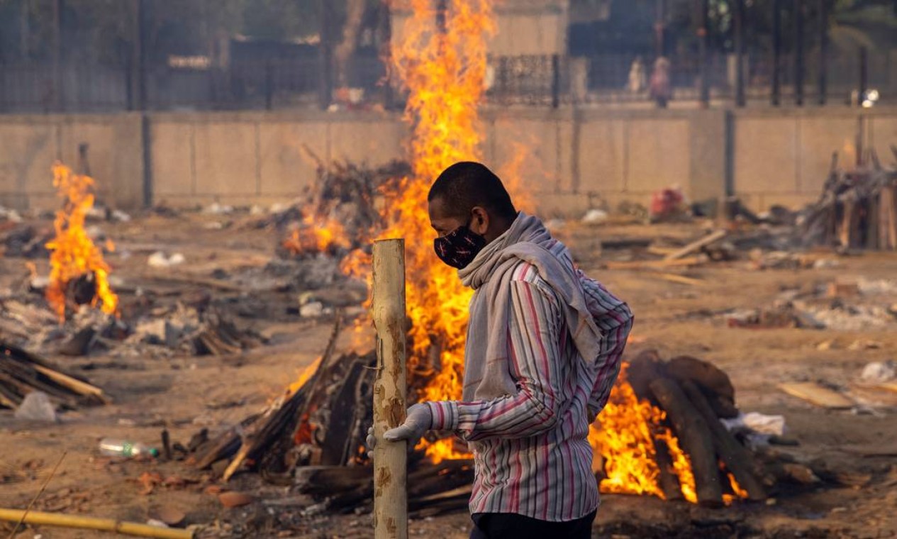 Homem passa por piras em um crematório em Nova Delhi, Índia Foto: Danish Siddiqui / REUTERS