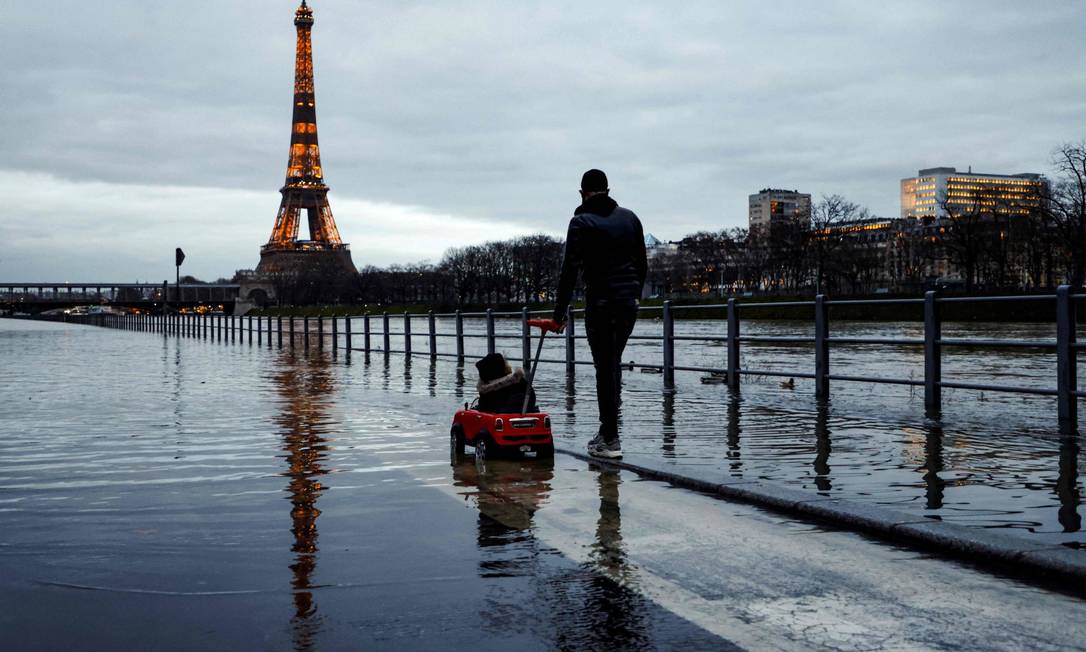 Homem passeia com criança em calçada alagada após o Rio Sena transbordar em Paris Foto: LUDOVIC MARIN / AFP/4-2-21
