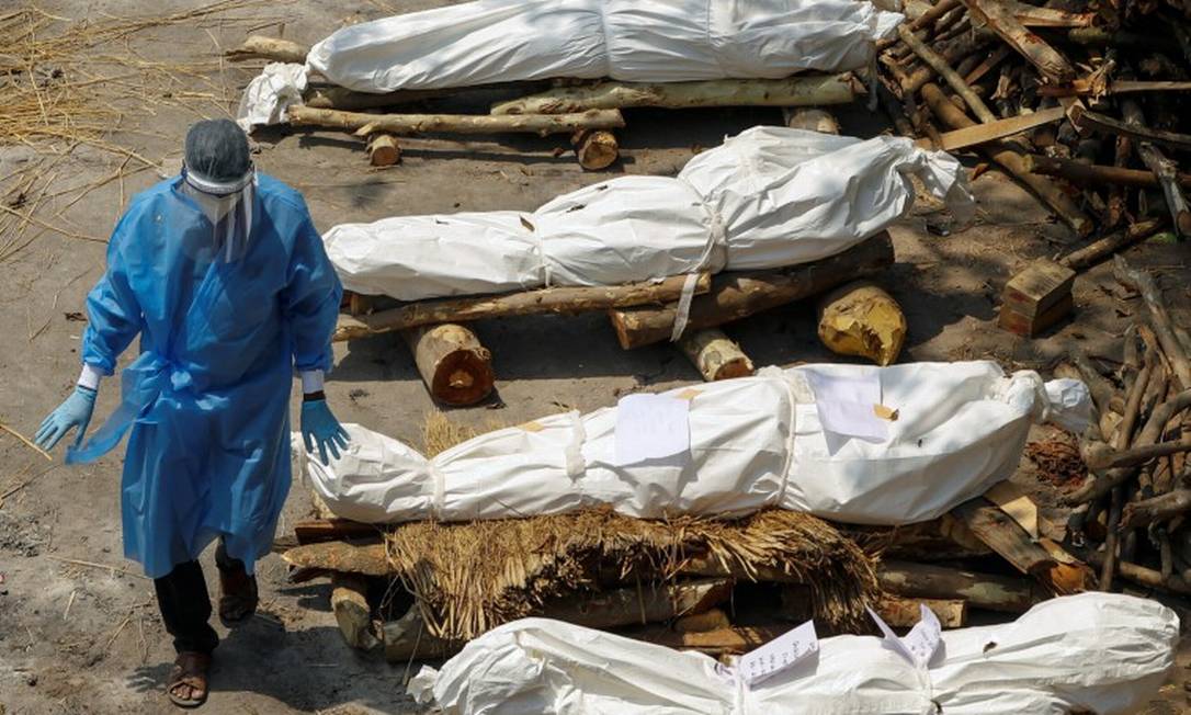 Com equipamento de proteção, trabalhador da saúde caminha por corpos de vítimas da Covid-19 esperando pela cremação Foto: ADNAN ABIDI / REUTERS