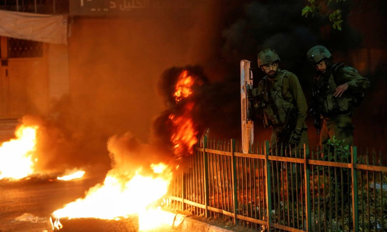 Soldados israelenses ficam ao lado de pneus em chamas enquanto palestinos participam de um protesto anti-Israel contra a tensão em Jerusalém, em Hebron, na Cisjordânia ocupada por Israel Foto: MUSSA ISSA QAWASMA / REUTERS - 25/04/2021