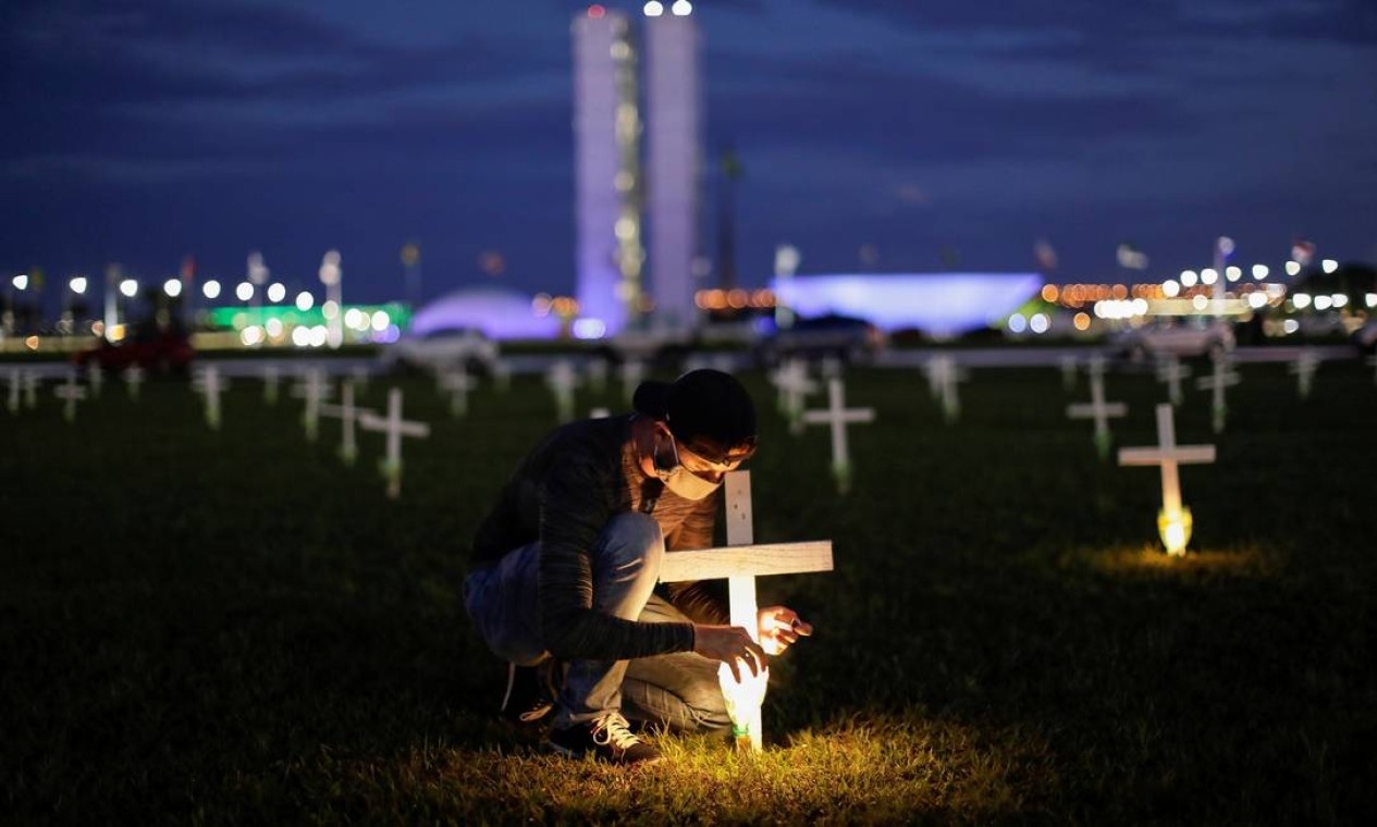 Homem acende uma vela ao lado de uma cruz simbolizando os que morreram por Covid-19, em frente ao Congresso Nacional, em Brasília Foto: Ueslei Marcelino - 27/04/2021 / Reuters