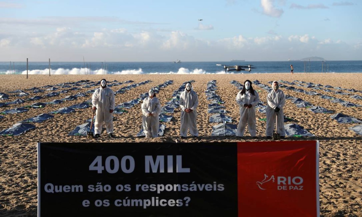 Uma faixa com os dizeres "400 mil, quem são os responsáveis e cúmplices?" é vista na frente de ativistas da ONG Rio de Paz usando máscaras e EPI enquanto exibem centenas de sacolas plásticas Foto: Pilar Olivares / Reuters