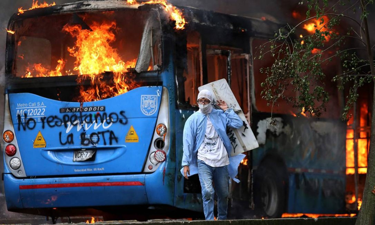 Homem caminha em frente a um ônibus de transporte público em chamas durante um protesto contra um projeto de reforma tributária lançado pelo presidente colombiano Iván Duque, em Cali Foto: PAOLA MAFLA / AFP