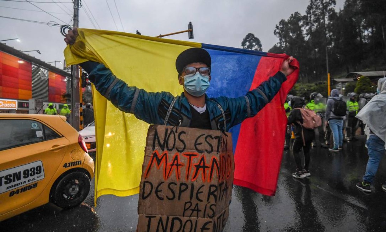 "Estão nos matando, desperta, país indolente", diz cartaz de manifestante que mar segurando bandeira nacional, em Bogotá Foto: JUAN BARRETO / AFP