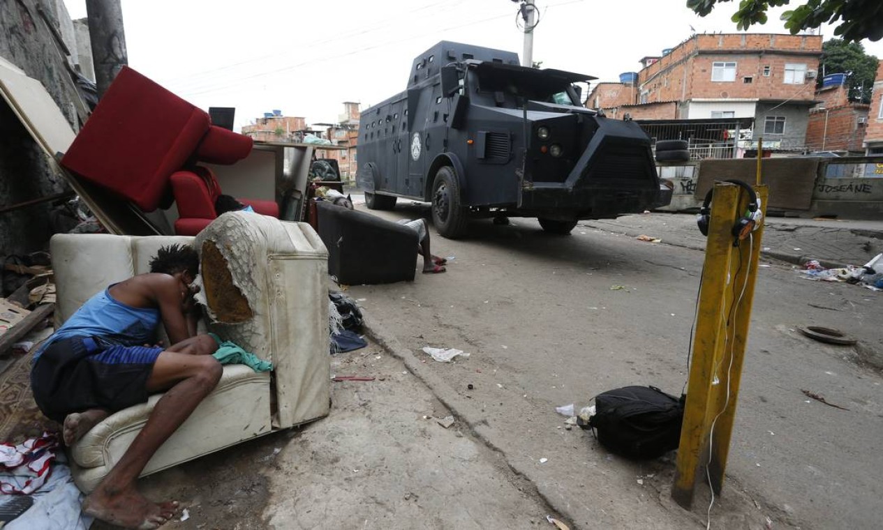 Pessoas em situação de rua dormem em mobília abandonada na rua enquanto passa o blindado da polícia Foto: Fabiano Rocha / Agência O Globo