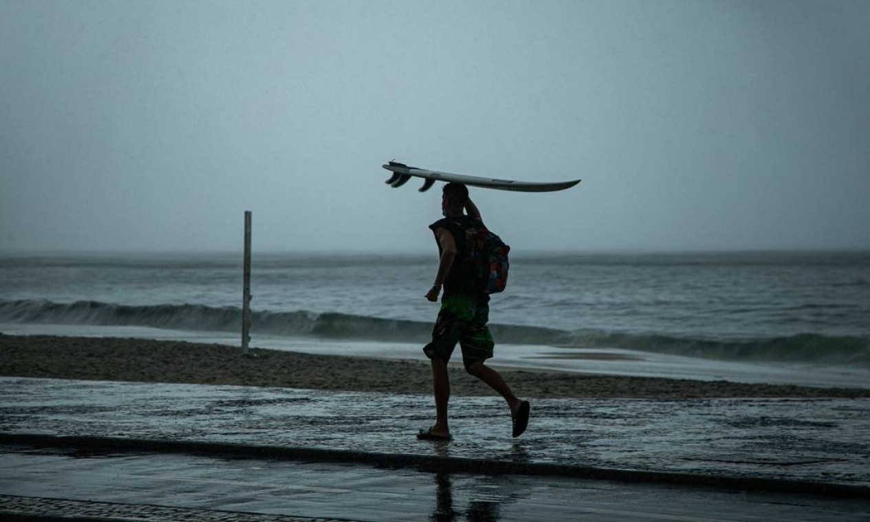 Surfista caminha na orla de Copacabana com prancha sobre a cabeça Foto: Hermes de Paula / Agência O Globo