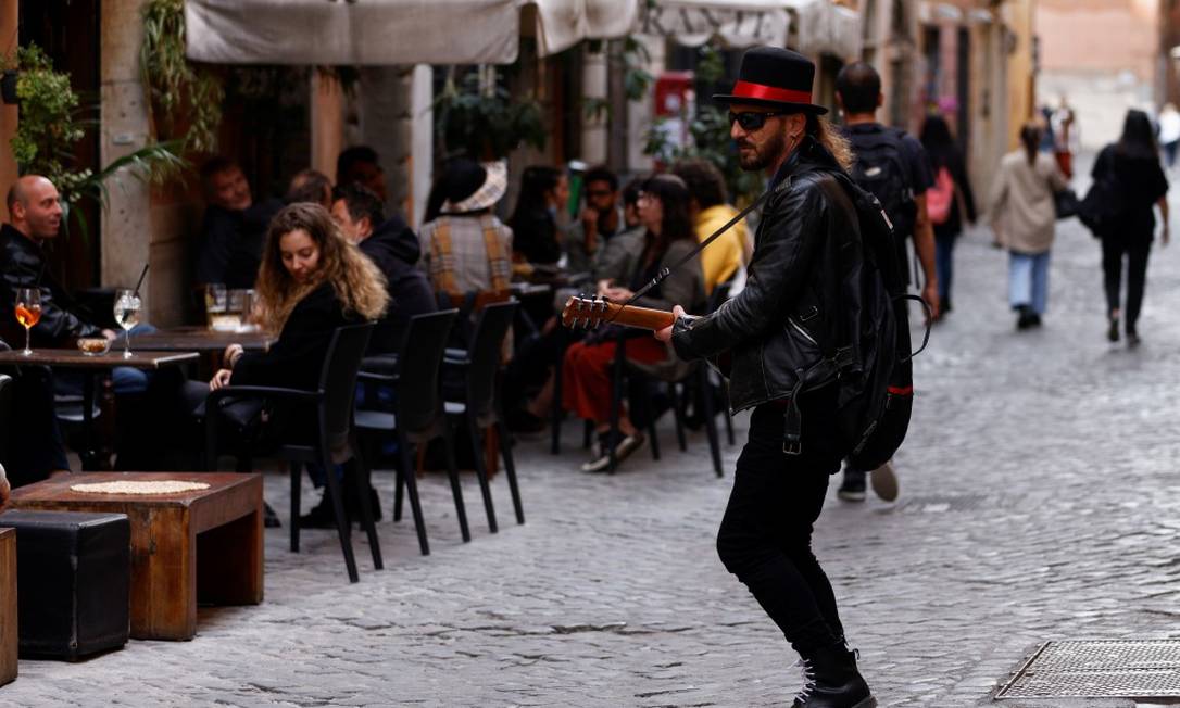 Homem toca violão em frente a fregueses de restaurantes em Roma; com o alívio das restrições, boa parte da Itália se tornou uma 'zona amarela' e restaurantes puderam voltar a servir clientes em espaços abertos Foto: GUGLIELMO MANGIAPANE / REUTERS/26-4-21