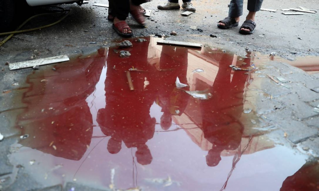 Pessoas são refletidas em uma poça de água misturada com sangue no local onde palestinos foram mortos em meio a uma explosão de violência israelense-palestina, no norte da Faixa de Gaza Foto: MOHAMMED SALEM / REUTERS