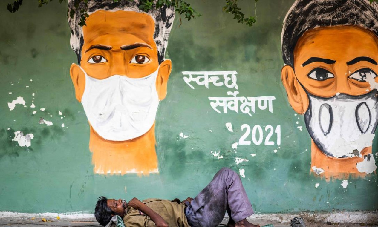 Homem descansa diante de pintura de conscientização sobre o coronavírus, em Nova Delhi, Índia Foto: JEWEL SAMAD / AFP