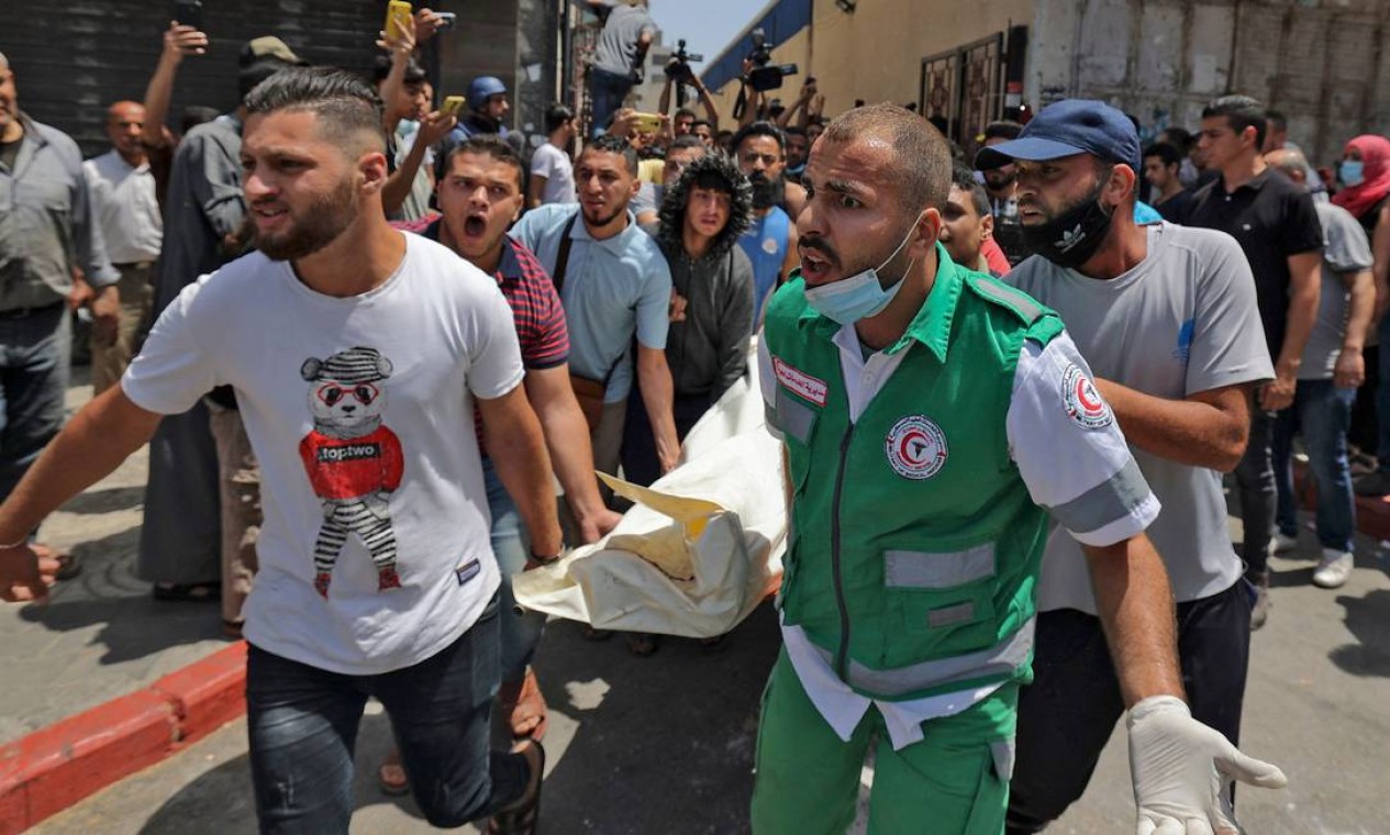 Voluntários e equipes de resgates da Palestina carregam corpo de local bombardeado por Israel Foto: MAHMUD HAMS / AFP