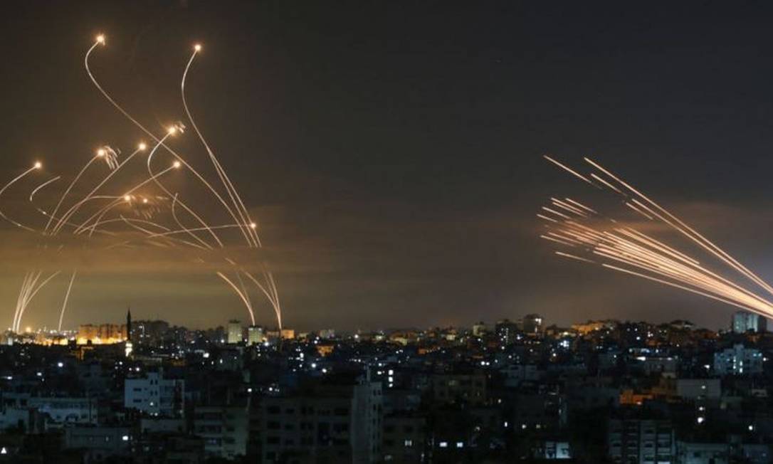 Os msseis israelenses,  esqueda, lanados para interceptar os foguetes do Hamas,  direita Foto: ANAS BABA/GETTY IMAGES