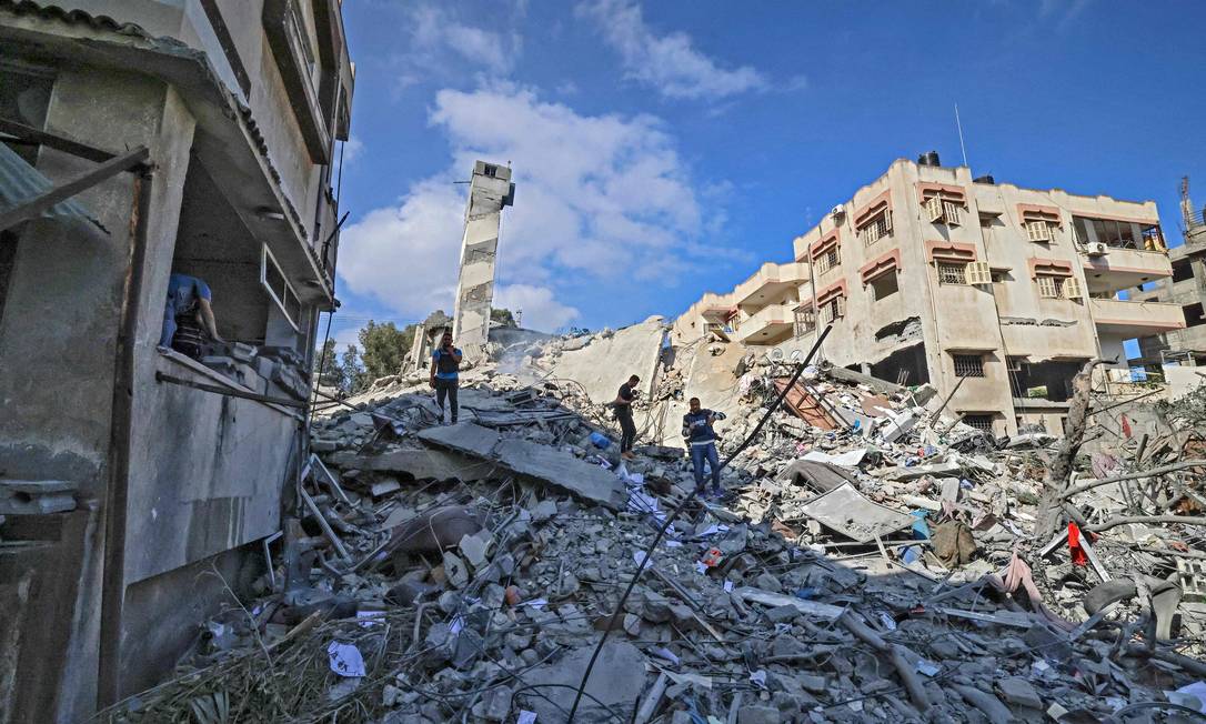 Palestinos andam pelos destroços de prédio destruído após ataque israelense na Faixa de Gaza em 18 de maio de 2021 Foto: Mahmud Hams / AFP