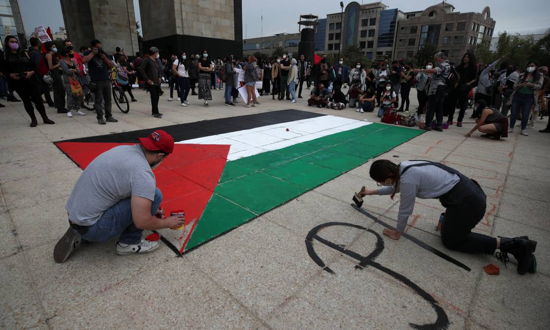 Um homem pinta uma bandeira palestina no chão perto do Monumento à Revolução enquanto uma mulher escreve "Palestina Livre", na Cidade do México, México Foto: HENRY ROMERO / REUTERS - 15/05/2021