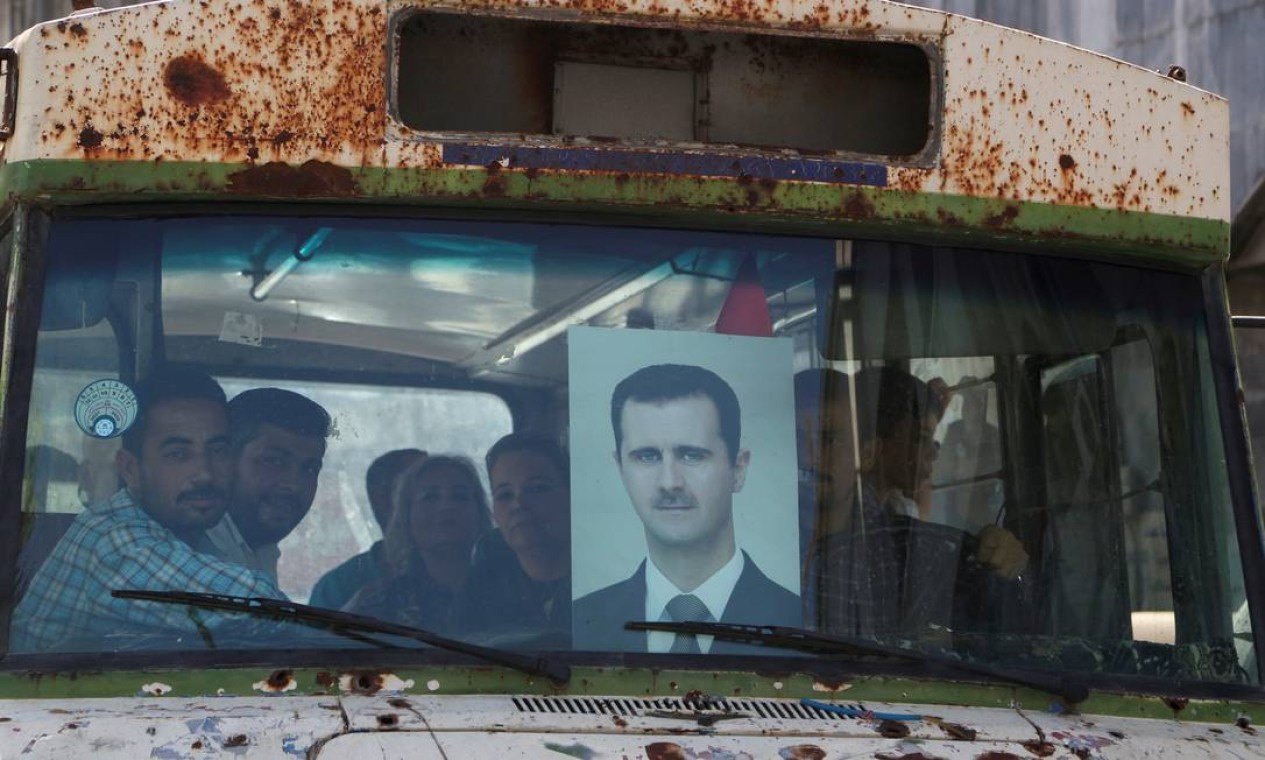 Pessoas viajam de ônibus a caminho de uma seção eleitoral para votar, durante as eleições presidenciais, em Damasco, Síria. No para-brisa, uma foto de Bashar al-Assad, presidente desde 2000 Foto: YAMAM AL SHAAR / REUTERS