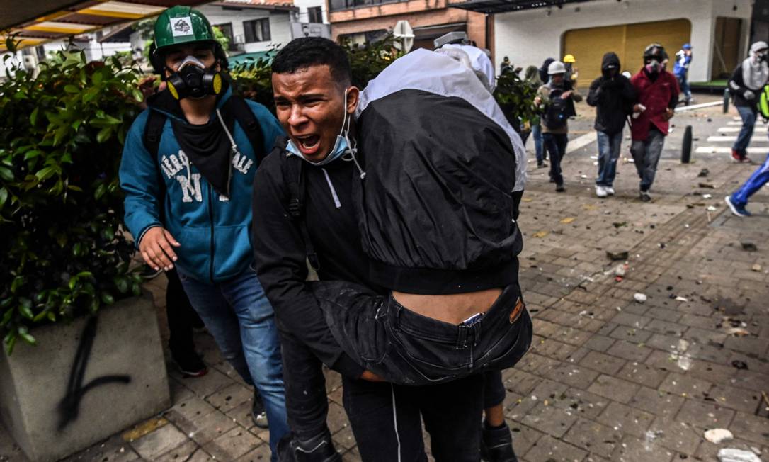 Um homem carrega um manifestante ferido durante confrontos com a polícia de choque em protesto em Medellín, Colômbia Foto: JOAQUIN SARMIENTO / AFP