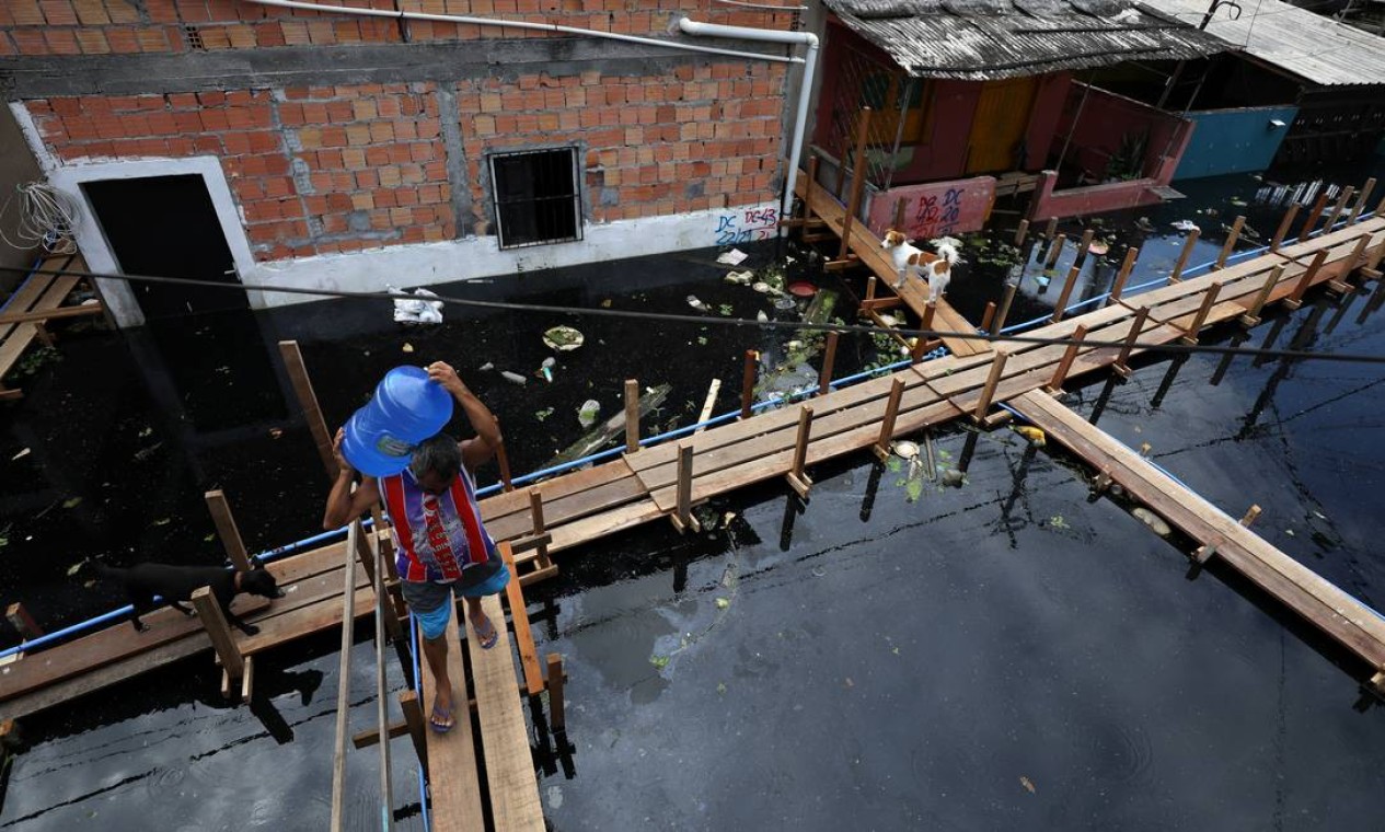 Um homem carrega um galão de água potável sobre um ponte improvisada em rua inundada pelo Rio Negro, no bairro de São Jorge, em Manaus Foto: BRUNO KELLY / REUTERS