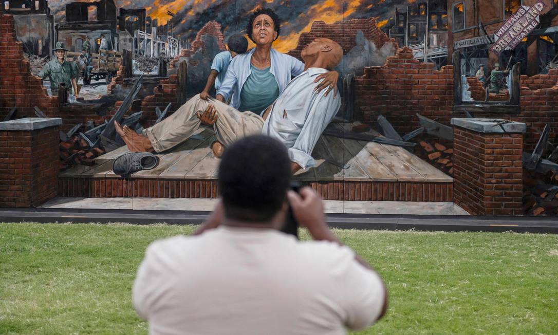 Um homem tira uma foto de mural em homenagem às vítimas do Massacre de Tulsa, em 1921 Foto: ANDREW CABALLERO-REYNOLDS / AFP