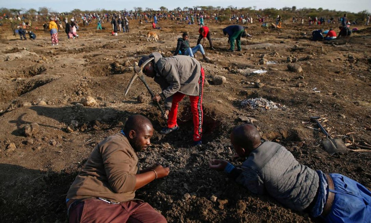 Homem usa uma picareta para cavar enquanto outros procuram o que acreditam ser diamantes, após a descoberta de pedras não identificadas na aldeia KwaHlathi perto de Ladysmith, África do Sul Foto: PHILL MAGAKOE / AFP