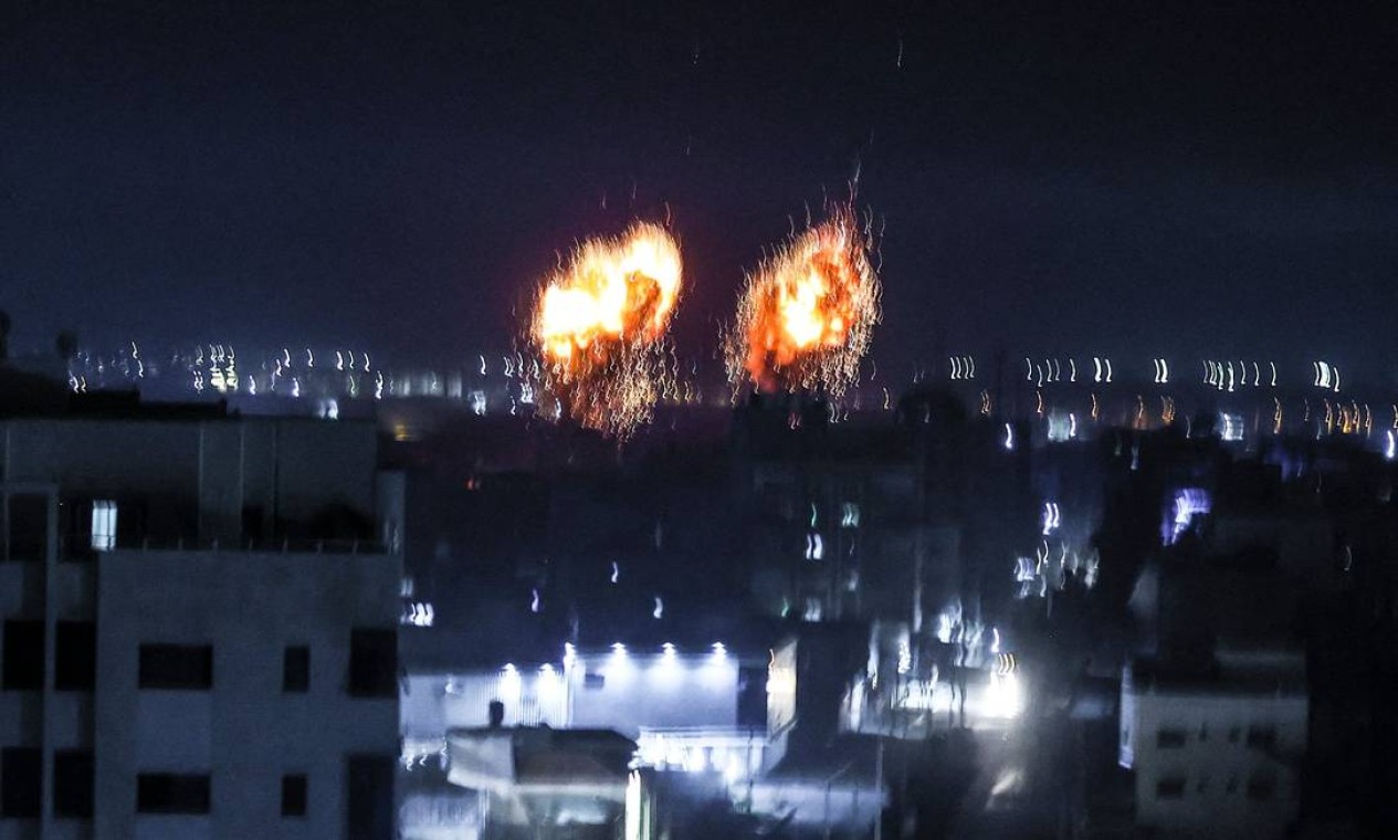 Explosões iluminam o céu noturno na Cidade de Gaza, enquanto as forças israelenses bombardeiam a Palestina Foto: MAHMUD HAMS / AFP