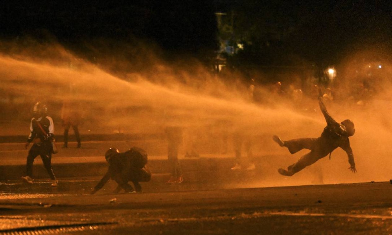 Um manifestante cai ao ser atingido por um canhão de água durante confrontos com a polícia de choque em meio aos protestos em andamento contra o governo do presidente colombiano Iván Duque, em Bogotá Foto: JUAN BARRETO / AFP