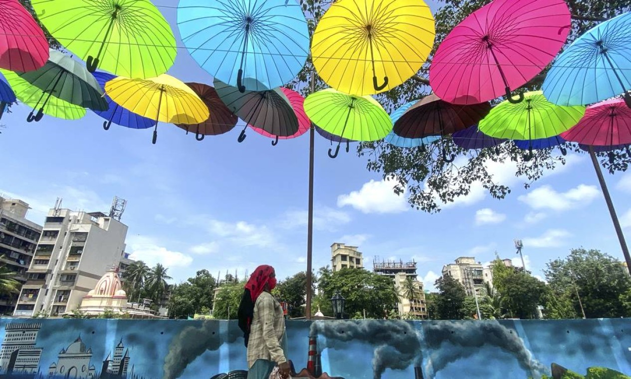 Mulher caminha sob uma instalação artística de guarda-chuvas coloridos enquanto o governo reduz as restrições em meio à pandemia de Covid-19, em Mumbai, Índia Foto: INDRANIL MUKHERJEE / AFP