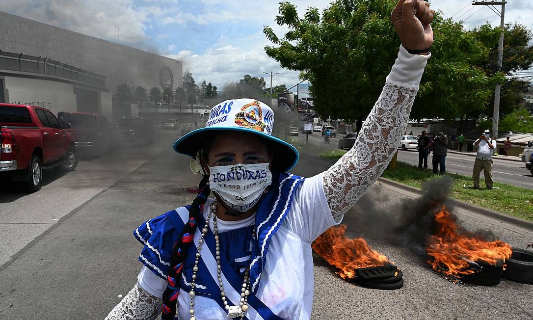 Una donna alza il pugno davanti a una barriera di pneumatici in fiamme durante una protesta contro le zone di lavoro e sviluppo economico (Zedes) - un nuovo tipo di divisione amministrativa - alla periferia della Banca centrale dell'Honduras, a Tegucigalpa, Foto: ORLANDO SIERRA / AFP