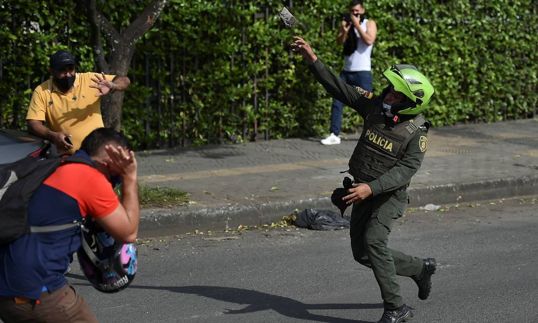 Policial arremessa uma pedra contra manifestantes durante protestos em Cali, na Colômbia Foto: LUIS ROBAYO / AFP