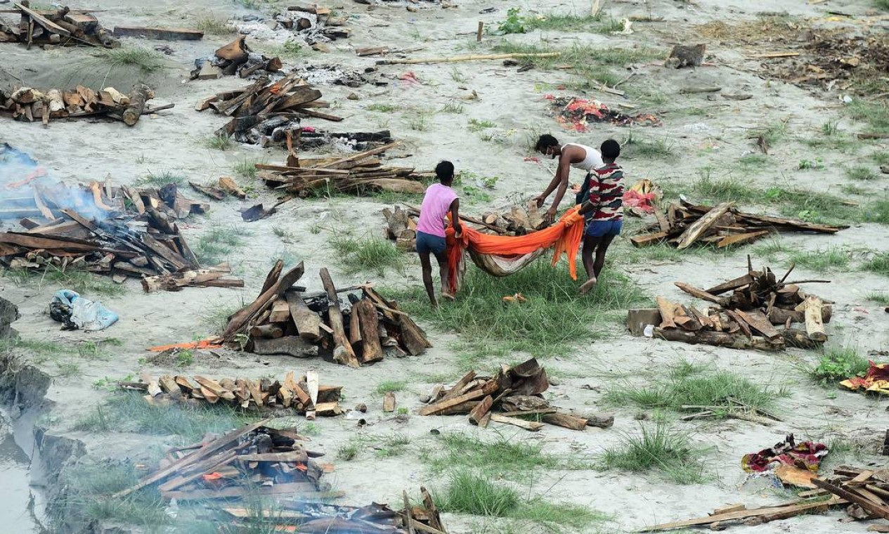 Funcionários de uma empresa municipal se preparam para cremar um corpo enterrado em uma cova rasa nas margens do rio Ganges, durante a pandemia de Covid-19, enquanto cremam outros corpos também enterrados lá para evitar que flutuem rio abaixo, conforme o nível da água aumenta perto de Phaphamau Ghat, em Allahabad, Índia Foto: SANJAY KANOJIA / AFP
