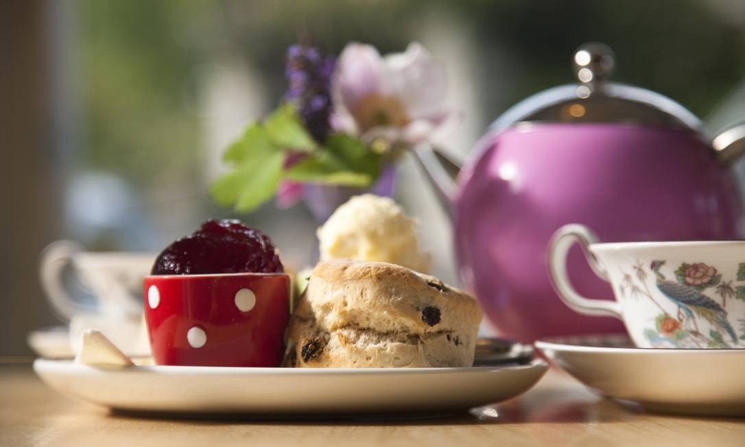 A traditional cream tea laid out on a table inside the Lustleigh Tearooms, with scones, jam and cream. A large pink teapot. Foto: ©VisitBritain/ David Clapp / Divulgação