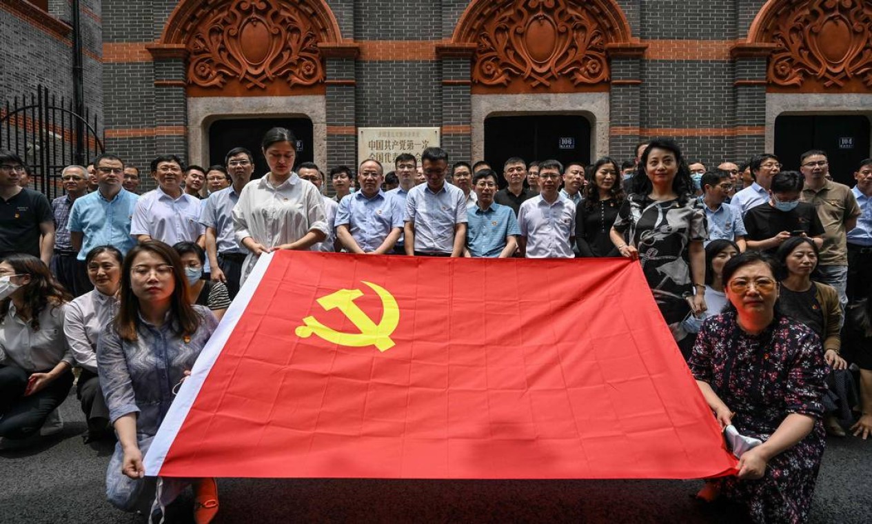Pessoas posam com bandeira do Partido Comunista da China ao lado do museu erguido onde foi realizado o primeiro congresso do Partido Comunista, em Xangai. Foto: HECTOR RETAMAL / AFP
