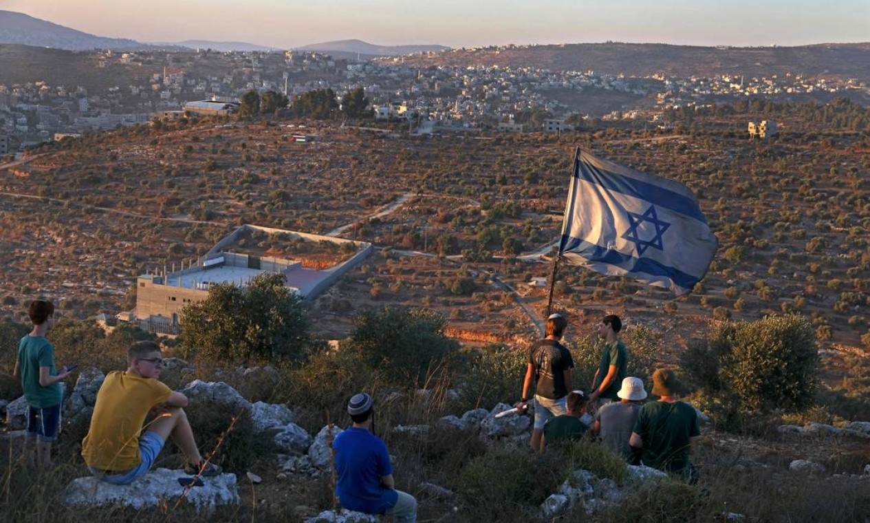 Jovens colonos israelenses erguem uma bandeira israelense no recém-estabelecido posto avançado de Eviatar, perto da cidade palestina de Nablus, na Cisjordânia ocupada Foto: MENAHEM KAHANA / AFP