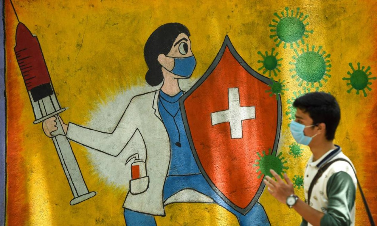 Estudante passa por um mural de parede que mostra um profissional de saúde usando uma máscara enquanto segura uma vacina e um escudo para divulgar a conscientização sobre o coronavírus Covid-19, em Mumbai, India Foto: PUNIT PARANJPE / AFP