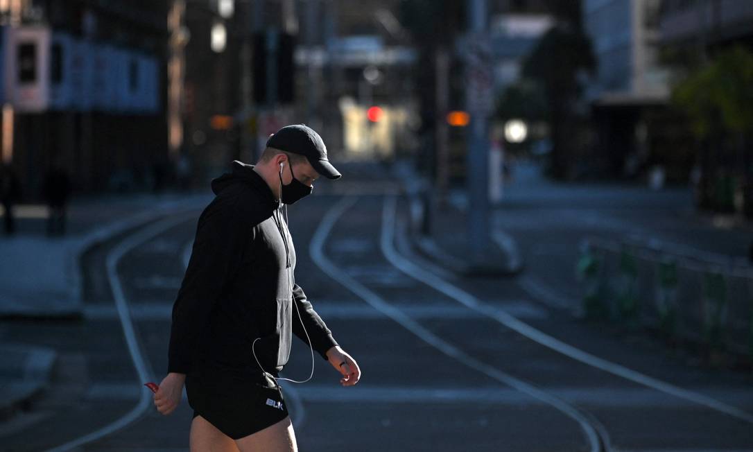 Homem usando máscara cruza os trilhos do bonde no distrito comercial central vazio de Sydney Foto: STEVEN SAPHORE / AFP
