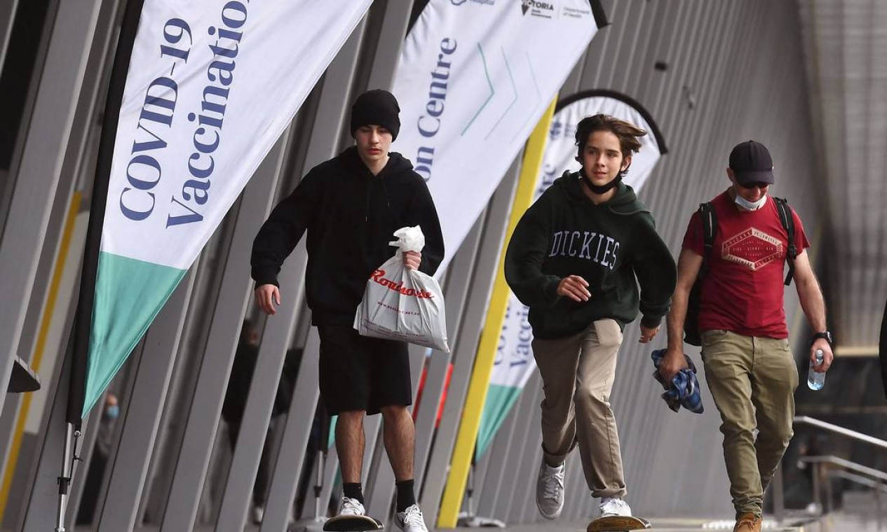 Jovens andando de skate lockpassam por um centro de vacinação Covid-19 em Melbourne Foto: WILLIAM WEST / AFP